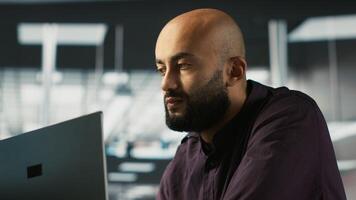 Smiling employee in warm office working on company project, multitasking. Cheerful freelancer answering emails, typing on keyboard, working in modern workplace, camera A close up video