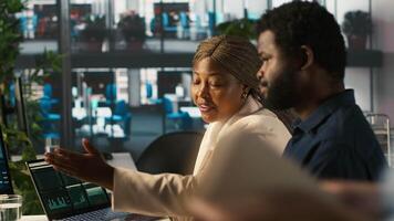 Supervisor in office discussing with employee about key performance indicators for revenue, profitability and operational efficiency. African american manager supervising employee at work, camera A video