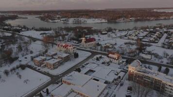 Snow covered town with a red roofed church and tall spire, intersected by roads. A partially frozen body of water and trees are visible in the background. video