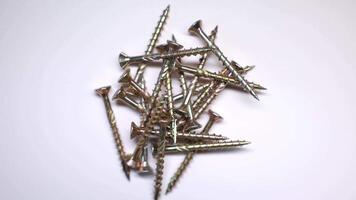 A scattered pile of golden metallic screws with threaded bodies and flat countersunk heads, displayed against a plain white background. video
