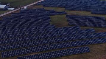 Rows of solar panels arranged in a grid cover a grassy field, with small utility buildings and a fence marking the boundary of the renewable energy site. video