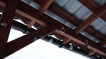 A wooden terrace with a metal roof and string lights, set against snow covered rooftops, trees, and a red brick building in a winter setting. video