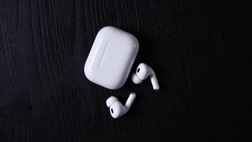 A pair of white wireless earbuds and a charging case with LED indicator are placed on a dark textured surface, emphasizing their sleek design. video