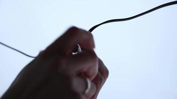 Close up of two hands screwing an LED bulb into black socket attached to a wire, set against a bright and minimal background. video