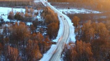 A rural road with light traffic winds through snow covered fields and sparse forests, featuring a small bridge over a narrow stream under warm sunlight. video