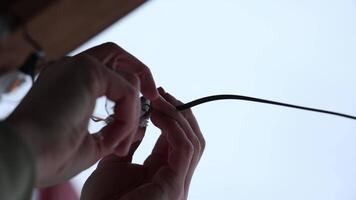 two hands screwing an LED bulb into a black socket attached to a wire, set against a bright and minimal background. video
