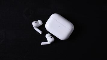 Pair of white wireless earbuds with matching charging case on a dark black surface, featuring compact design and LED indicator on the case. video