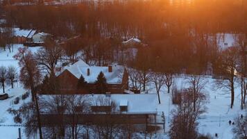 A snow covered scene with a red brick building, white roofed structure, leafless trees, and warm sunset light contrasting with the winter setting. video