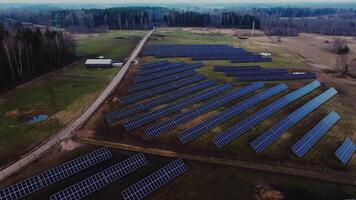 Systematic rows of solar panels in an open field with sparse vegetation, a small building, a water channel, and leafless trees in the background. video