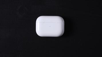 A white, rectangular wireless earbud charging case with rounded edges and a small LED indicator light, set against a solid black background. video