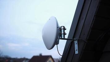 A white circular Wi Fi router is mounted on a wooden house exterior with visible cables and a metal bracket, set against a bright, partly cloudy sky. video