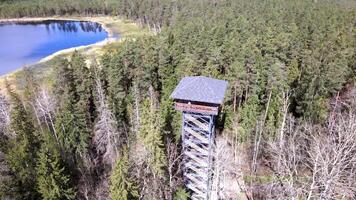 A tall wooden observation tower with a pitched roof and latticework stands amidst a forest of evergreen and deciduous trees under a clear sky. video