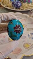 Crafting a traditional Ukrainian pysanka, an Easter egg using the beeswax technique, showcases intricate folk patterns in vibrant turquoise and red colors. video