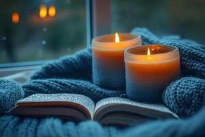 Two lit candles beside an open book, enveloped in a cozy knitted blanket, creating a warm, serene atmosphere. photo