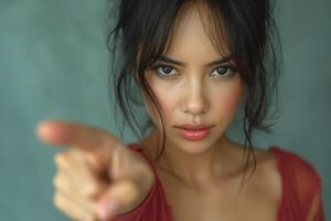 A striking young woman with medium skin tone points assertively at the viewer, showcasing a fierce and determined expression. photo