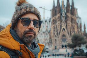 A ruggedly handsome man with a beard wears a beanie and sunglasses in front of an iconic architectural masterpiece. photo
