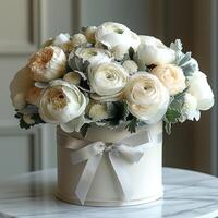 Elegant white floral arrangement in a round container, adorned with a satin bow, perfect for special occasions. photo