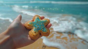 A hand holds a colorful star-shaped cookie against a serene beach backdrop, evoking a fun summertime vibe. photo