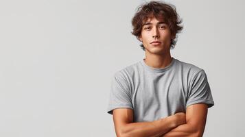 A young Hispanic man with curly hair stands confidently with crossed arms, wearing a gray t-shirt against a neutral backdrop. photo