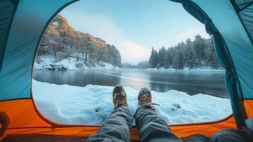A cozy winter scene featuring a person relaxing in a tent by a snow-covered lake, surrounded by frosty trees. photo