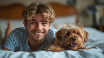 A smiling young Caucasian man relaxing on a bed with his playful dog, creating a cozy and joyful atmosphere. photo