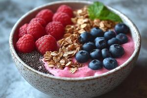 A beautiful bowl of vibrant smoothie topped with fresh blueberries, raspberries, granola, chia seeds, and a sprig of mint. photo