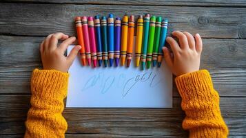 A child's hands, wearing a cozy yellow sweater, grasp colorful crayons over a blank sheet of paper, ready for creativity. photo