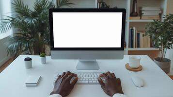 A Black man types on a sleek computer keyboard in a modern workspace filled with plants and natural light. photo