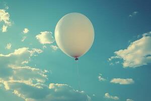 A single white balloon floats in a clear blue sky, surrounded by fluffy clouds, evoking feelings of freedom and joy. photo