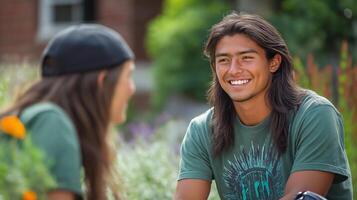 Smiling young Hispanic man enjoying a conversation outdoors with a friend, surrounded by lush greenery and vibrant flowers. photo