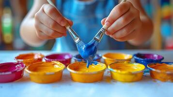 A child's hands mixing vibrant blue paint with colorful paints in small containers, fostering creativity and artistic expression. photo