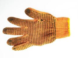 A wellworn orange work glove, showcasing its textured surface and darkcolored grip dots, lies against a clean white background. The image evokes themes of hard work, manual labor, and resilience. photo
