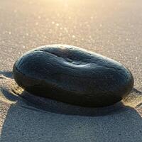 Polished dark stone on sandy beach at sunrise photo
