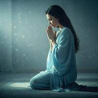 Praying woman in serene blue robe, dimly lit room photo