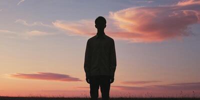 Silhouette of a man standing in a field at sunset. photo