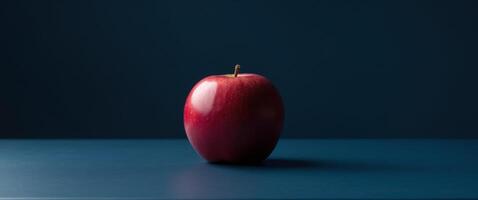 A single ripe red apple resting on a dark blue table. photo