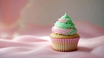 A whimsical cupcake with swirls of pink and green frosting sits gracefully on a gentle pink surface. photo