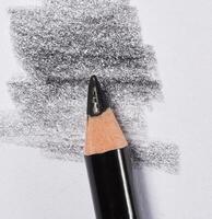 Close up of a sharpened black pencil with visible graphite shading on white paper photo