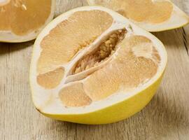 Fresh, juicy slice of pomelo fruit with visible pulp and peel. Citrus fruit section on wooden table. photo