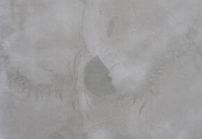 Close-up of a gray concrete wall with rough texture and irregular patterns. The surface has a natural, industrial photo