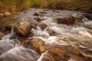 The water flows over numerous large, rounded rocks, creating a sense of movement and energy. photo