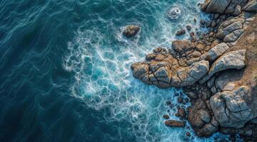 The ocean is blue and has a rocky shoreline. The waves are crashing against the rocks. The water is choppy and the rocks are scattered throughout the area. photo