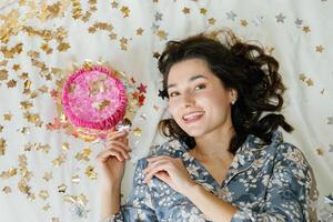 Young Woman Lying on Bed with Birthday Cake and Confetti photo