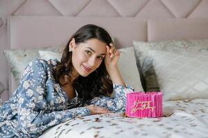 Woman celebrating birthday lying on bed with cake and balloons. photo