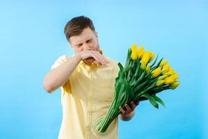 Man holding bunch of yellow flowers and sneezes from the smell. photo