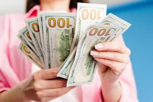 Close-up of female hands counting stack of hundred dollar bills blue background photo
