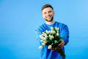 Man holding bouquet of tulips, looking at camera isolated on blue background. Celebration concept photo