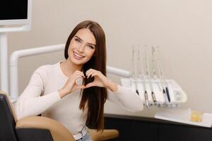 Patient is smiling and gesturing hands heart in dentist office. photo