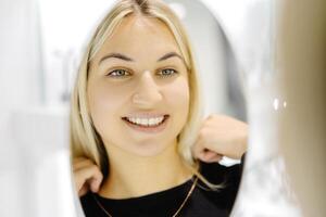 Smiling blonde woman trying a necklace in front of a mirror photo