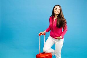 Traveler woman holding a suitcase handle, standing isolated on blue background studio photo